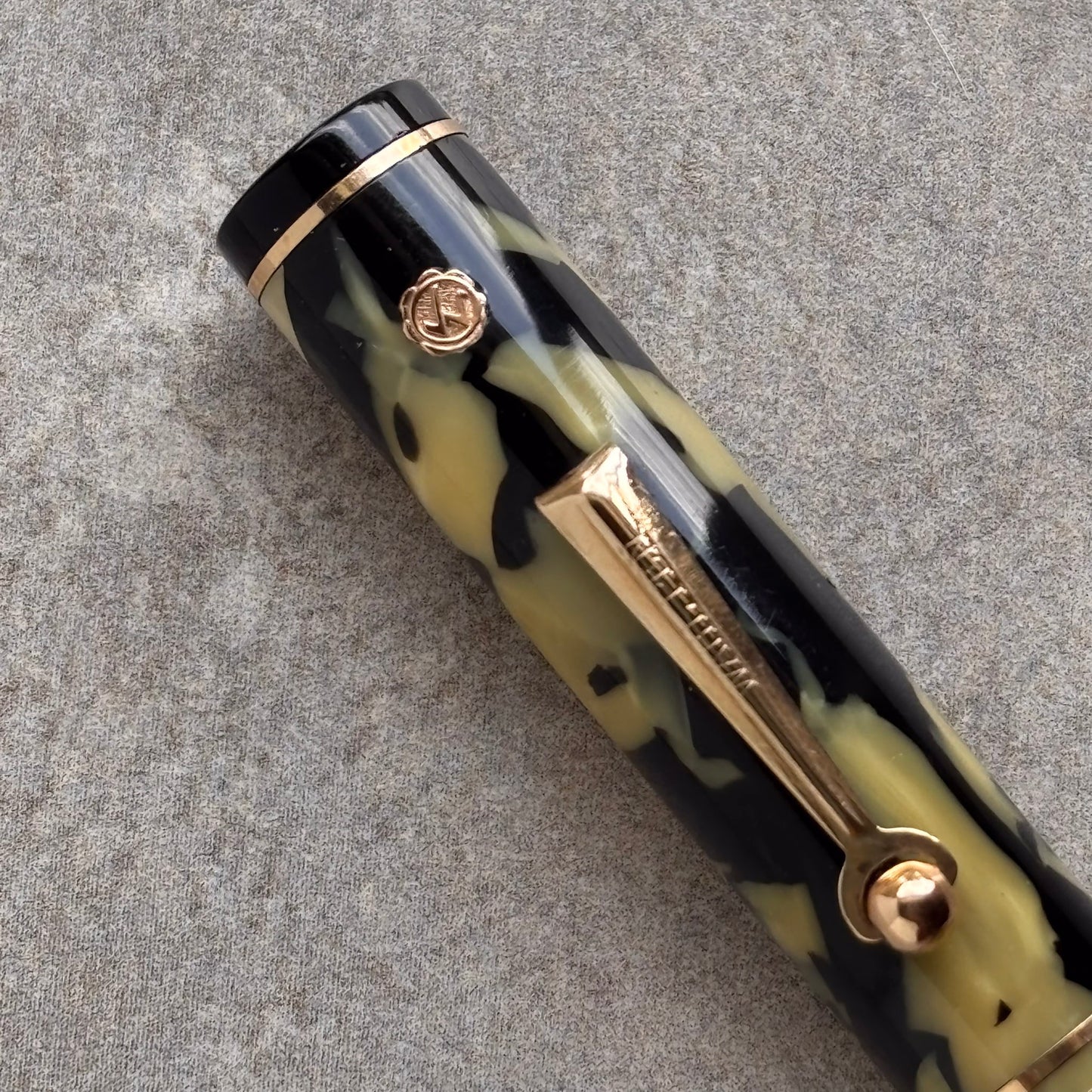 Camouflage-patterned pen with gold accents on a gray surface