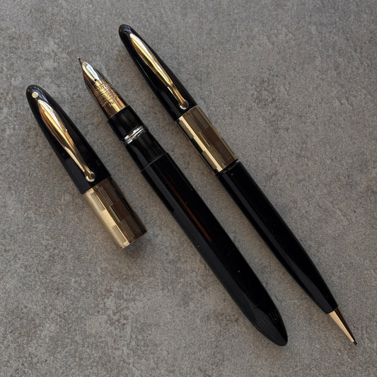 Two black and gold fountain pens on a gray surface