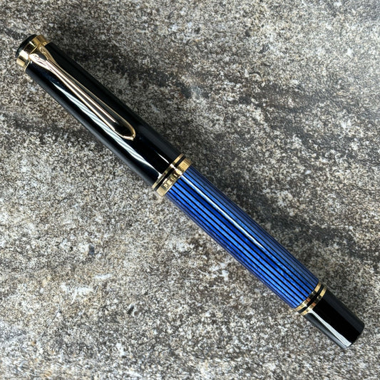 Pelikan M600 Blue/Black. Medium two tone nib, piston filler. Name/Type: Pelikan M600 Length: 5 1/4 Filling System: Piston Filler Color/Pattern: Blue/Black Nib Type/Condition and remarks: Medium 14K two tone nib The pen is in excellent condition, used but