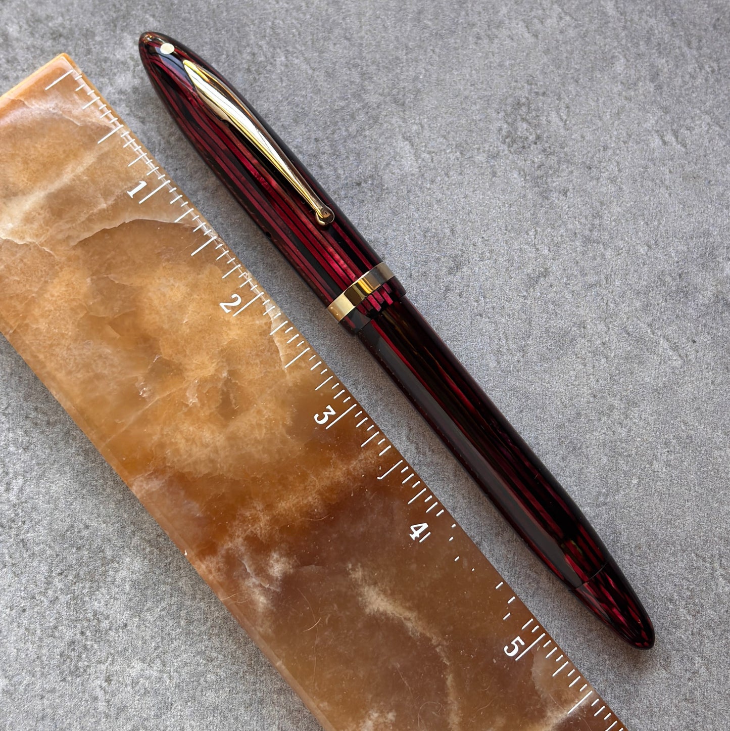 Red and gold pen on a brown stone surface with a ruler