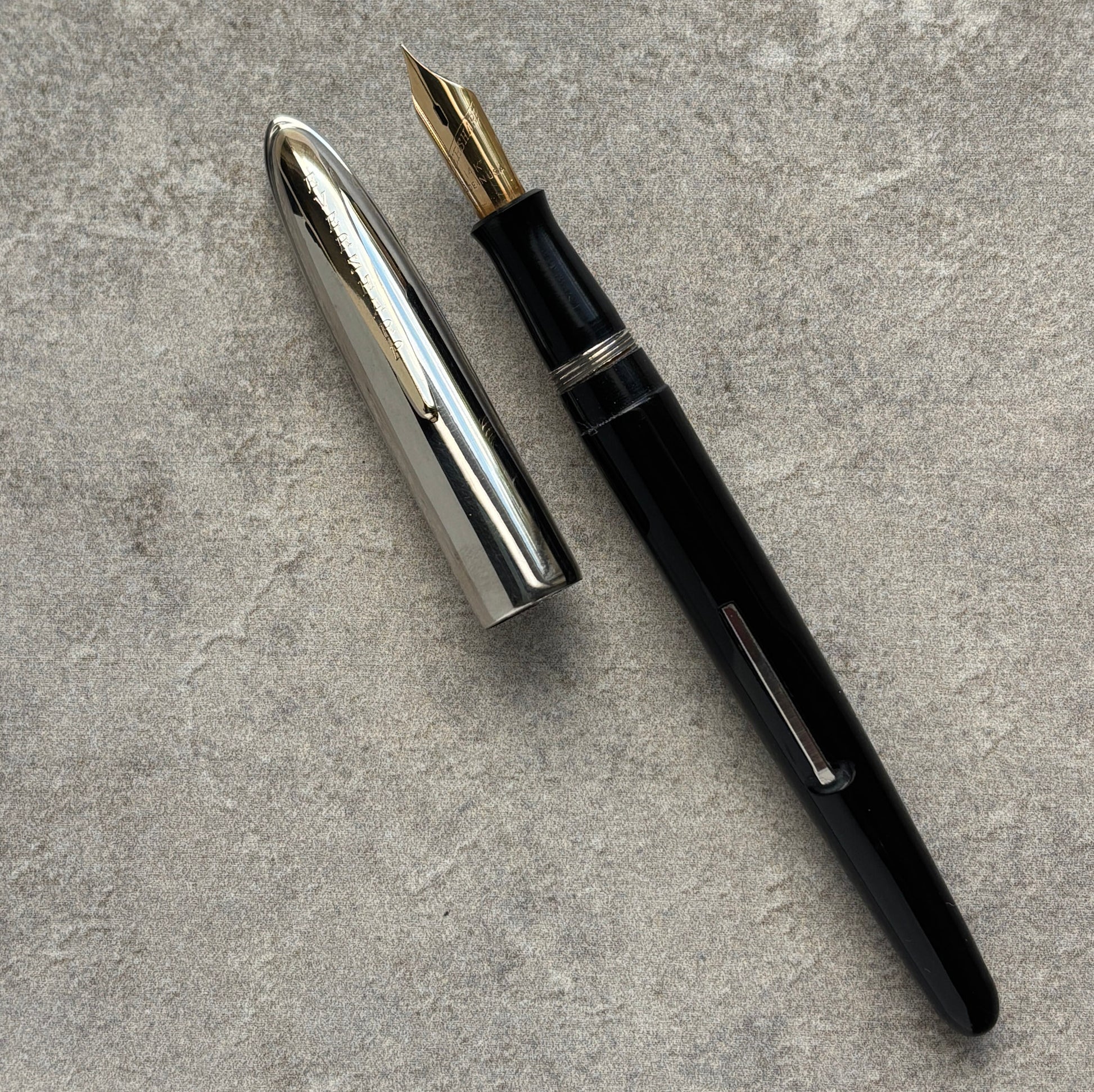 Black fountain pen with silver cap on a gray textured surface