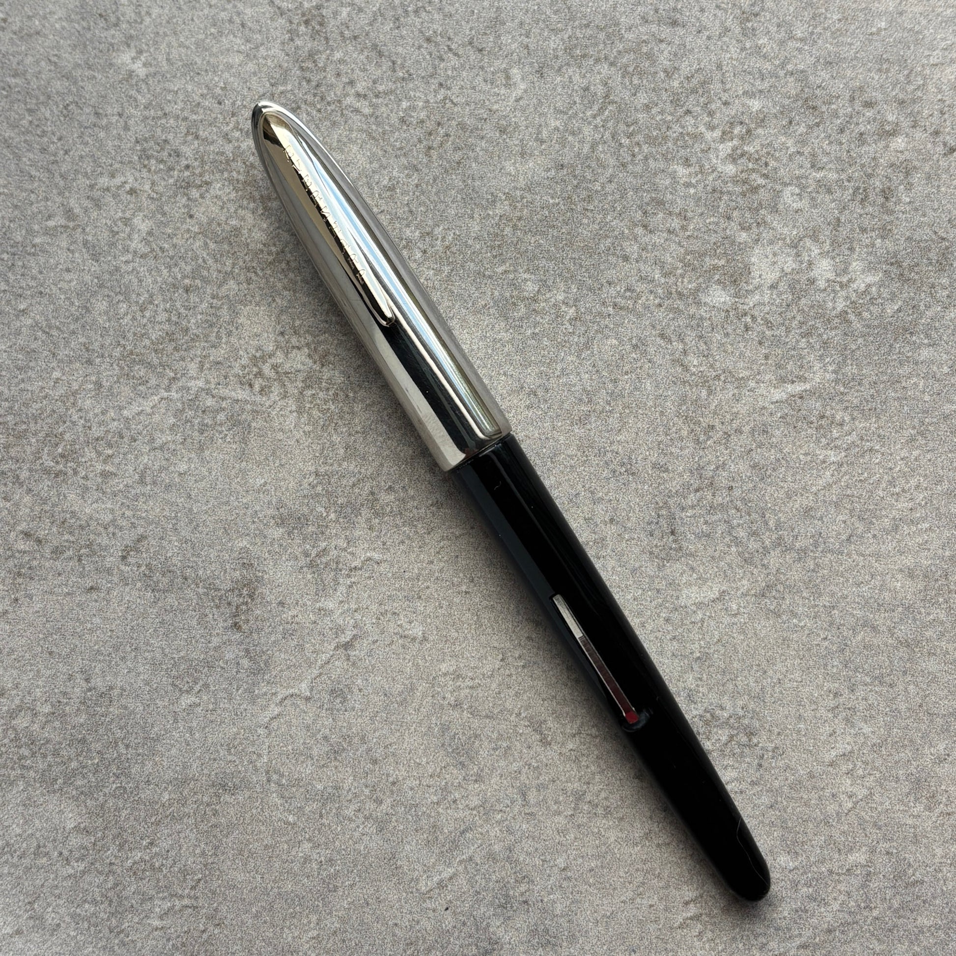 Black pen with silver cap on a gray concrete surface