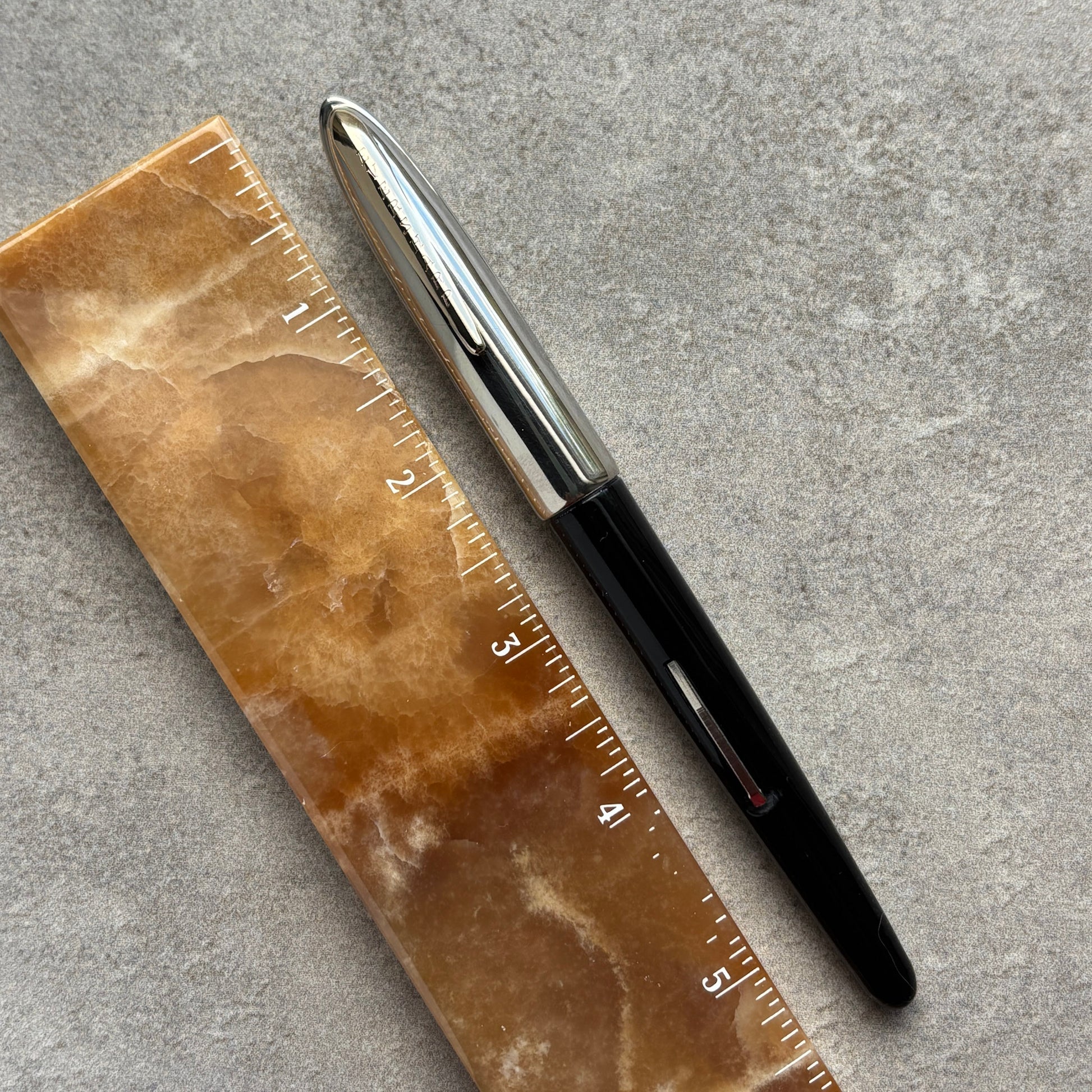 Black pen next to a brown ruler on a gray surface
