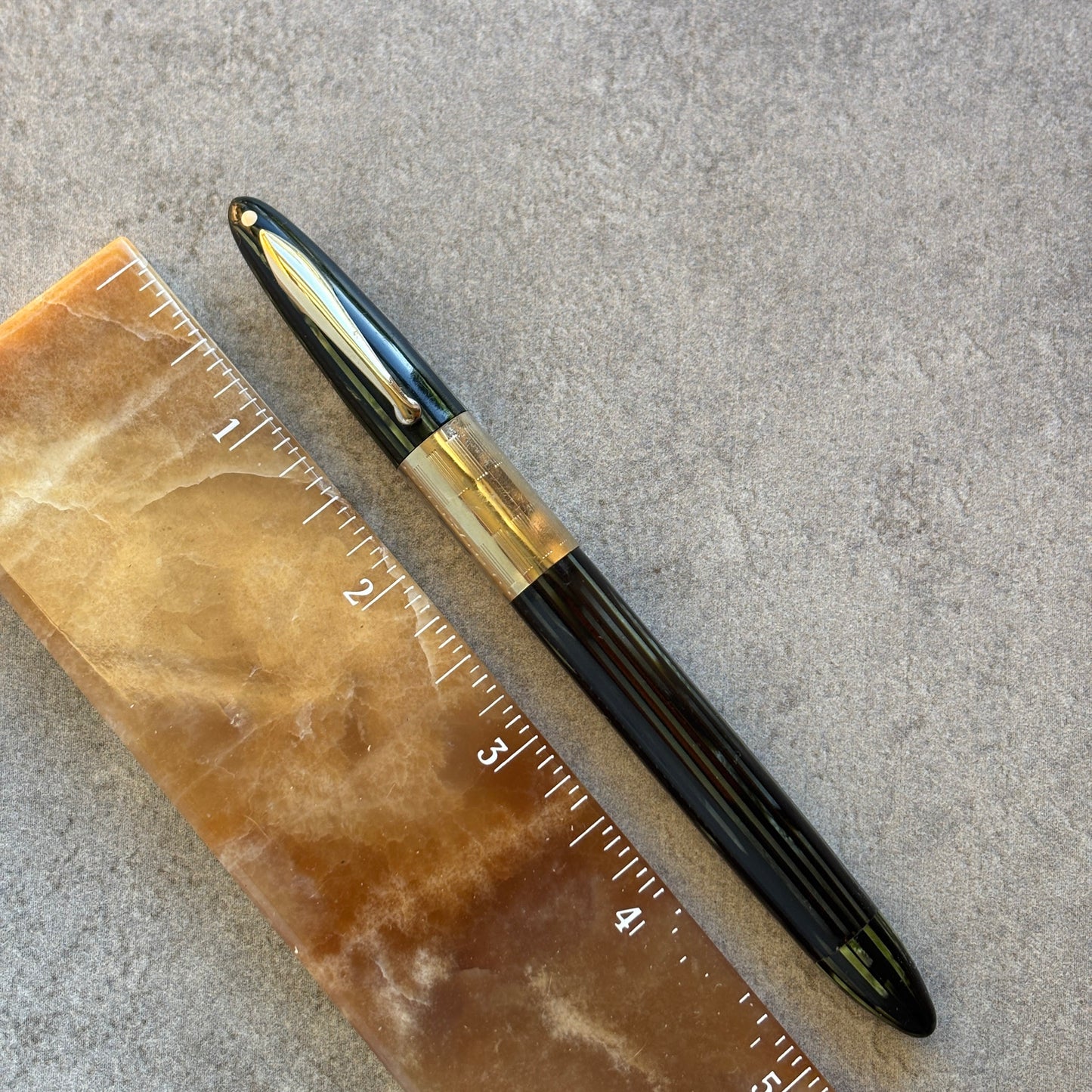 green and gold pen next to a ruler on a textured surface