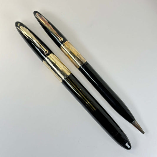 Sheaffer Triumph Vac-fil, Extra-wide cap Band, Black Fountain Pen and Pencil Set, Gold-filled trim, Medium Two-tone Nib Length: 5 1/8 Filling System: Vacuum-Fil; restored with new seals Color/Pattern: Black with gold-filled trim Nib Type/Condition and rem