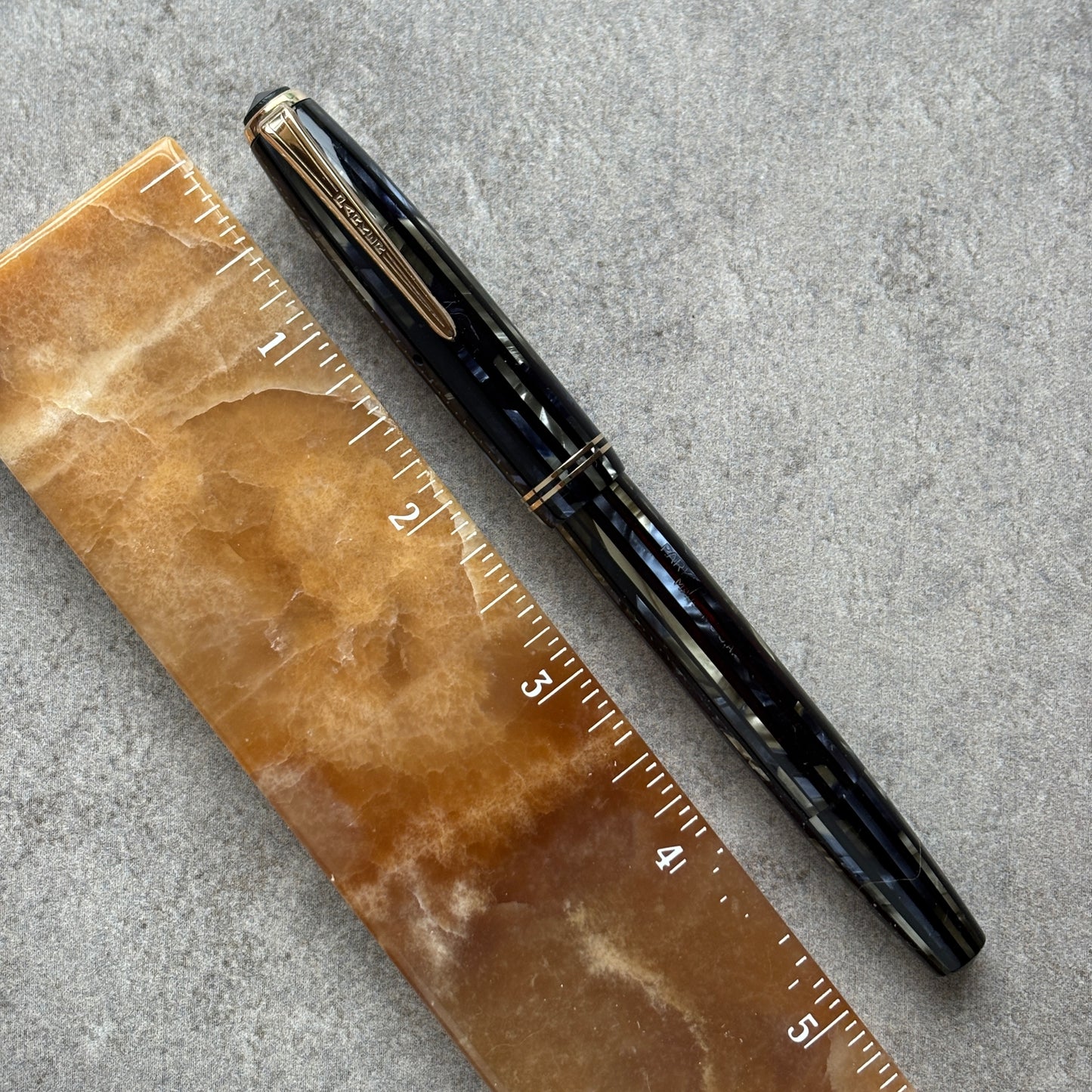 Black and blue pen next to a brown marble ruler on a gray surface
