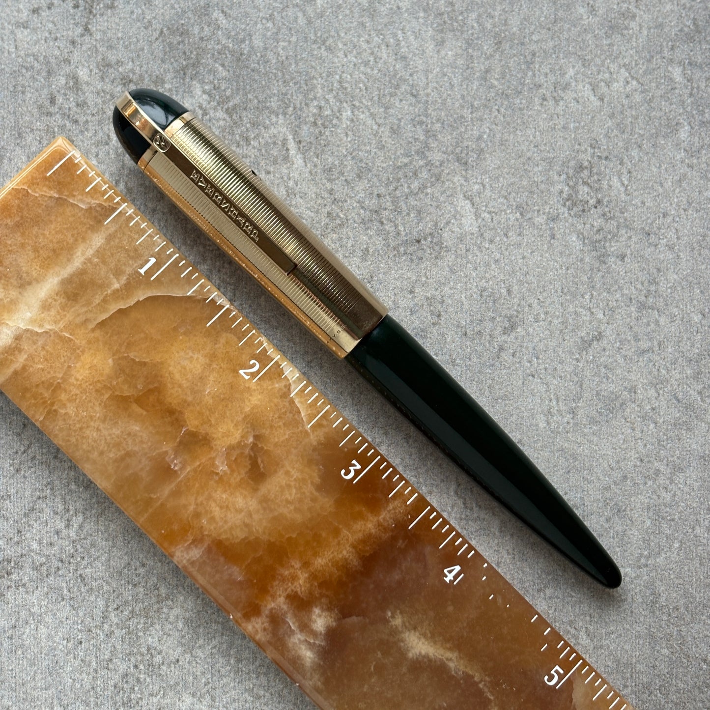 Pen with gold and black accents on a marble surface with a ruler for scale.