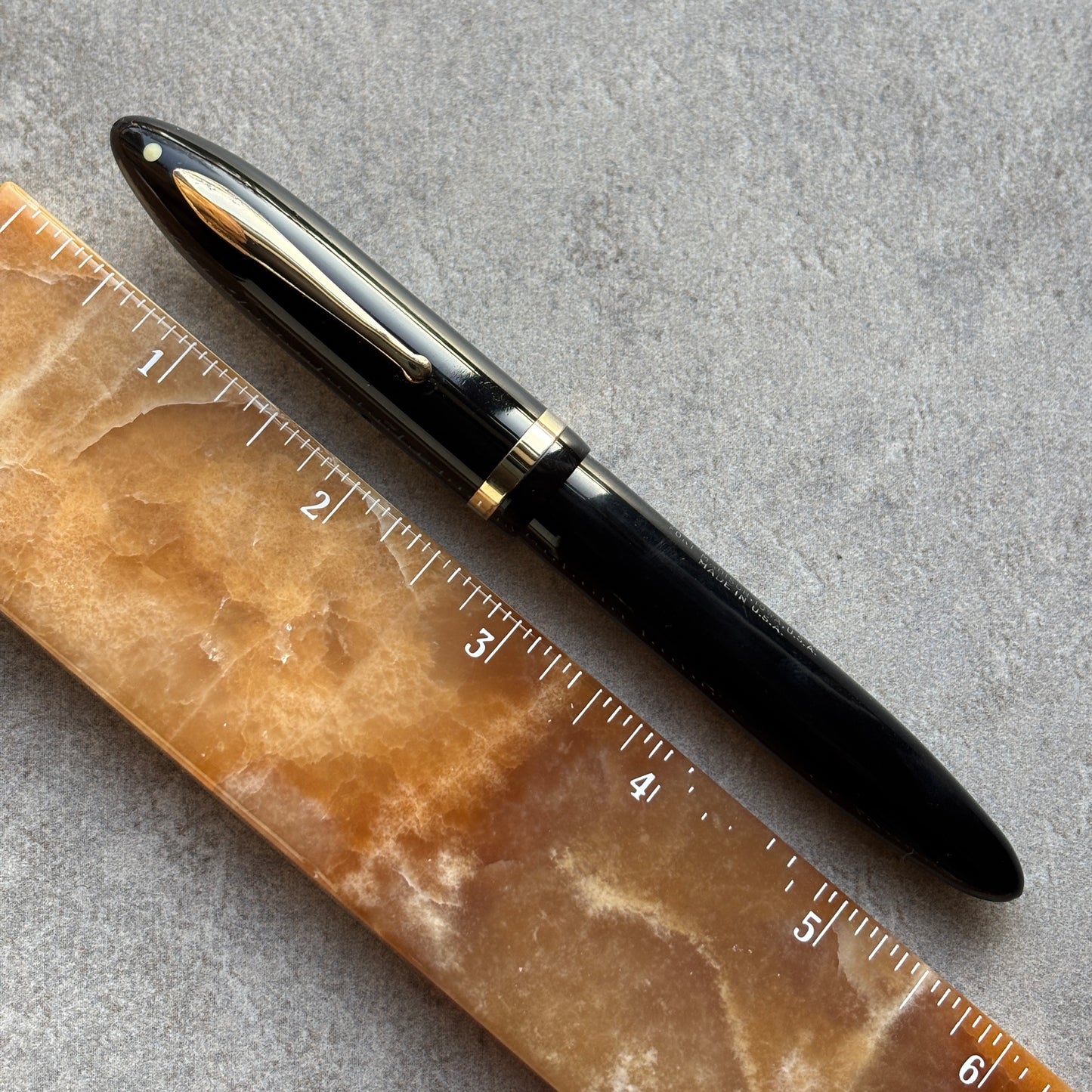 Black pen on a marble surface with a ruler for scale