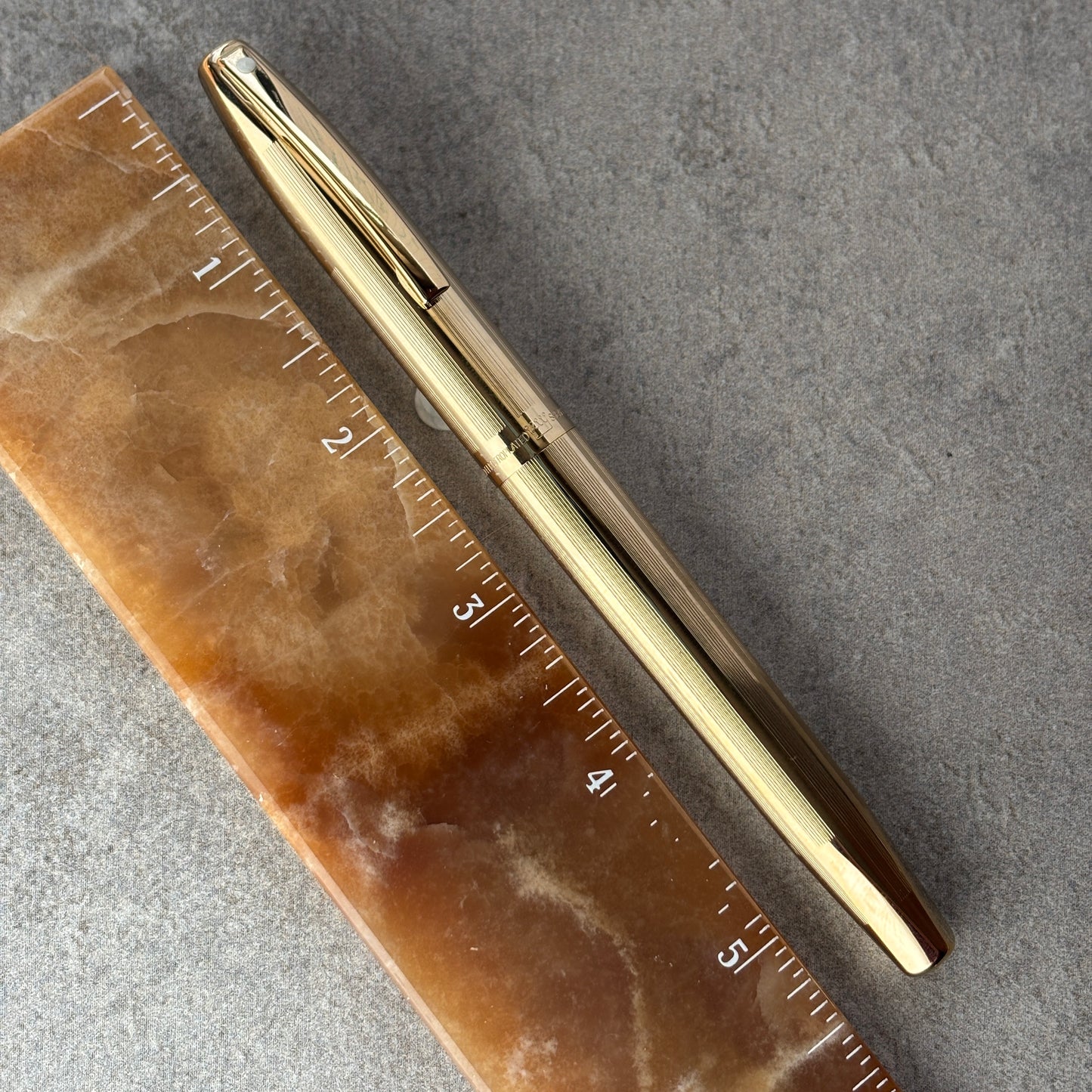 Gold pen next to a ruler on a gray surface