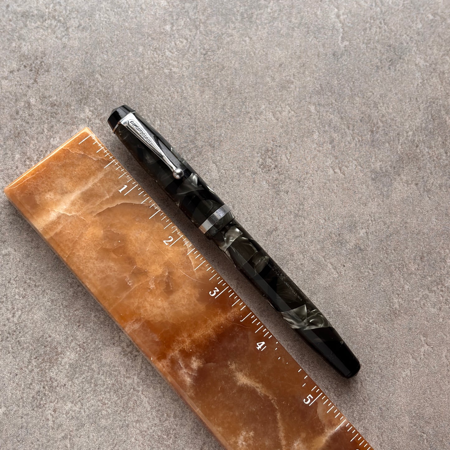 Parker Black pen on a brown marble ruler against a gray concrete background