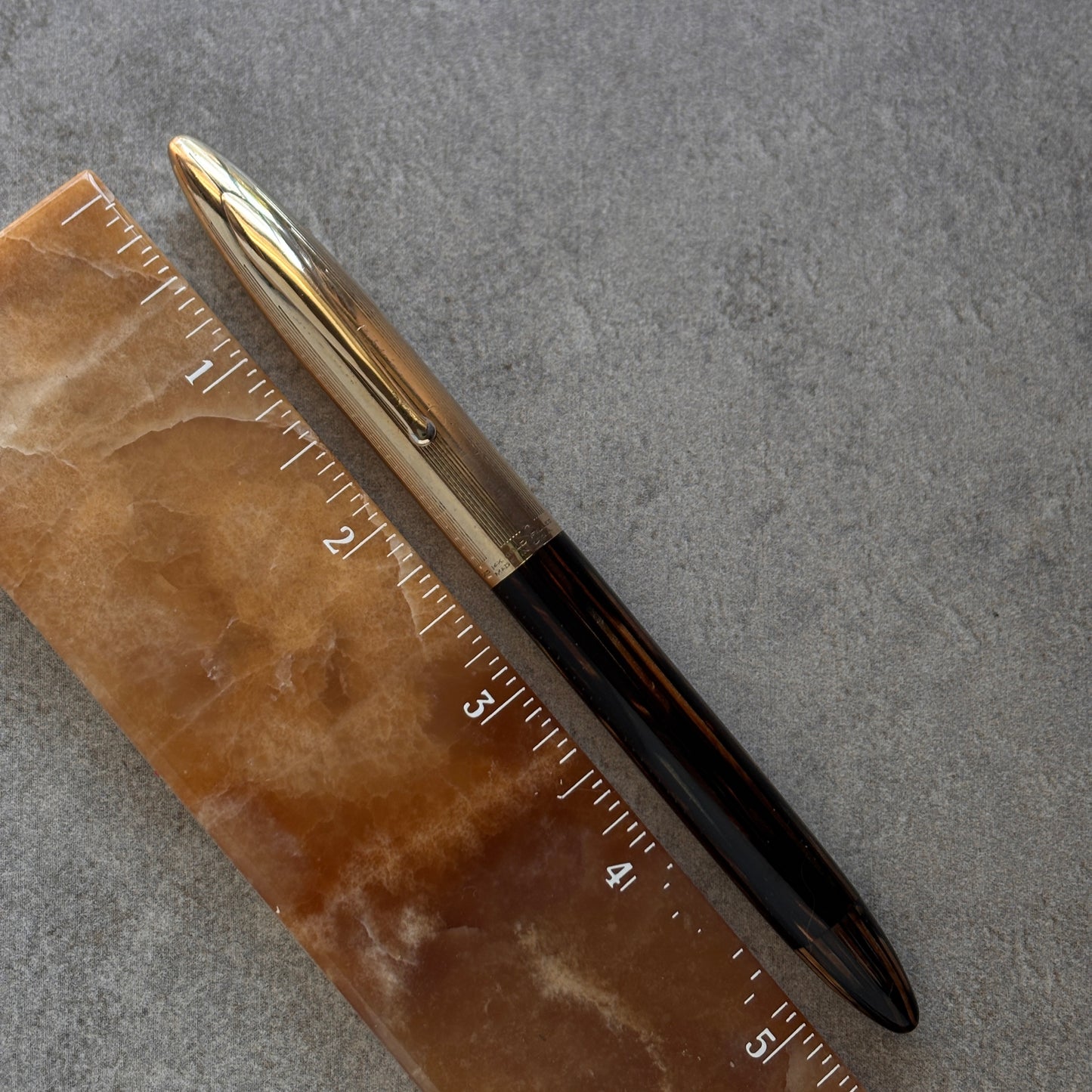 Pen with gold cap and black body on a marble surface with ruler