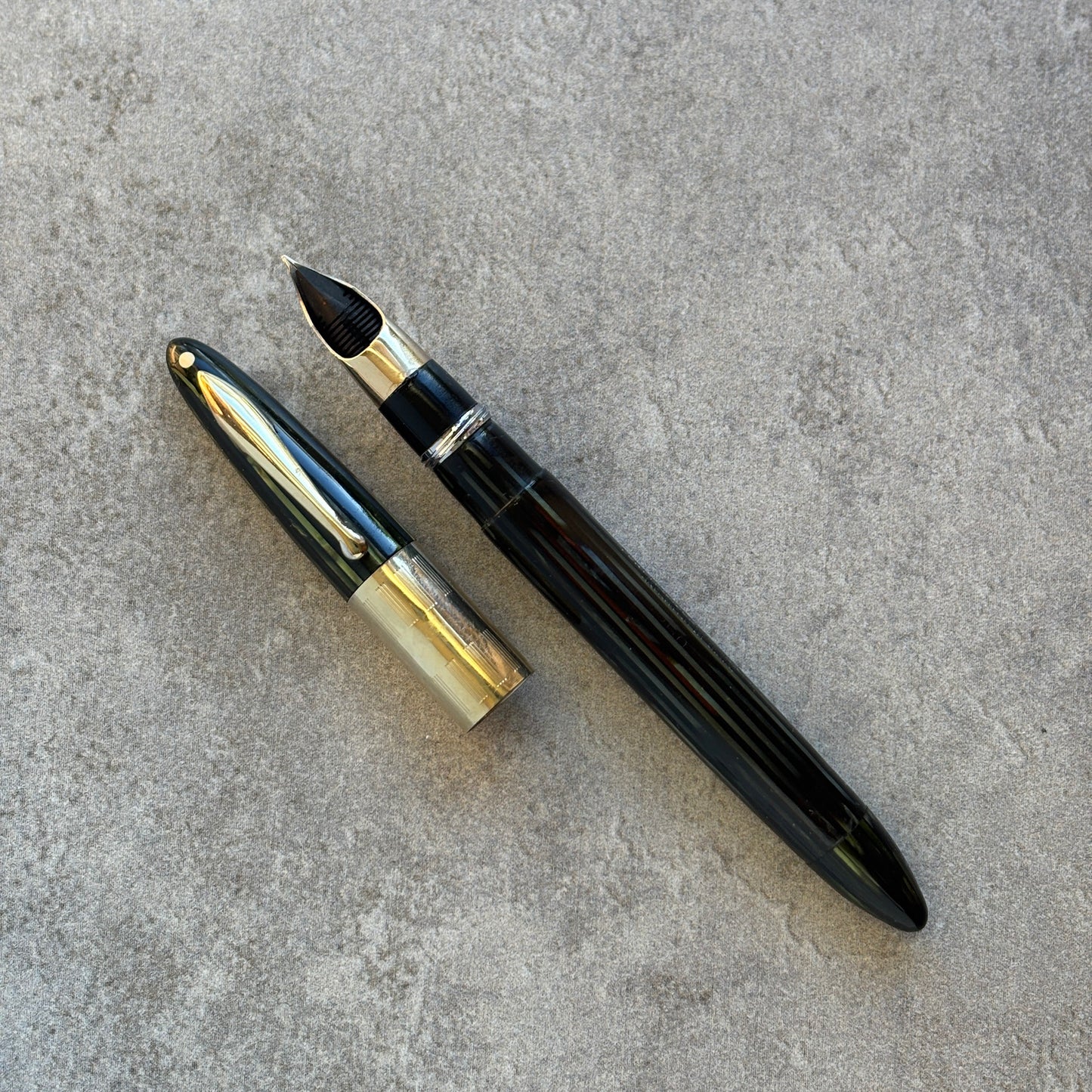 green and gold fountain pen on a gray concrete surface