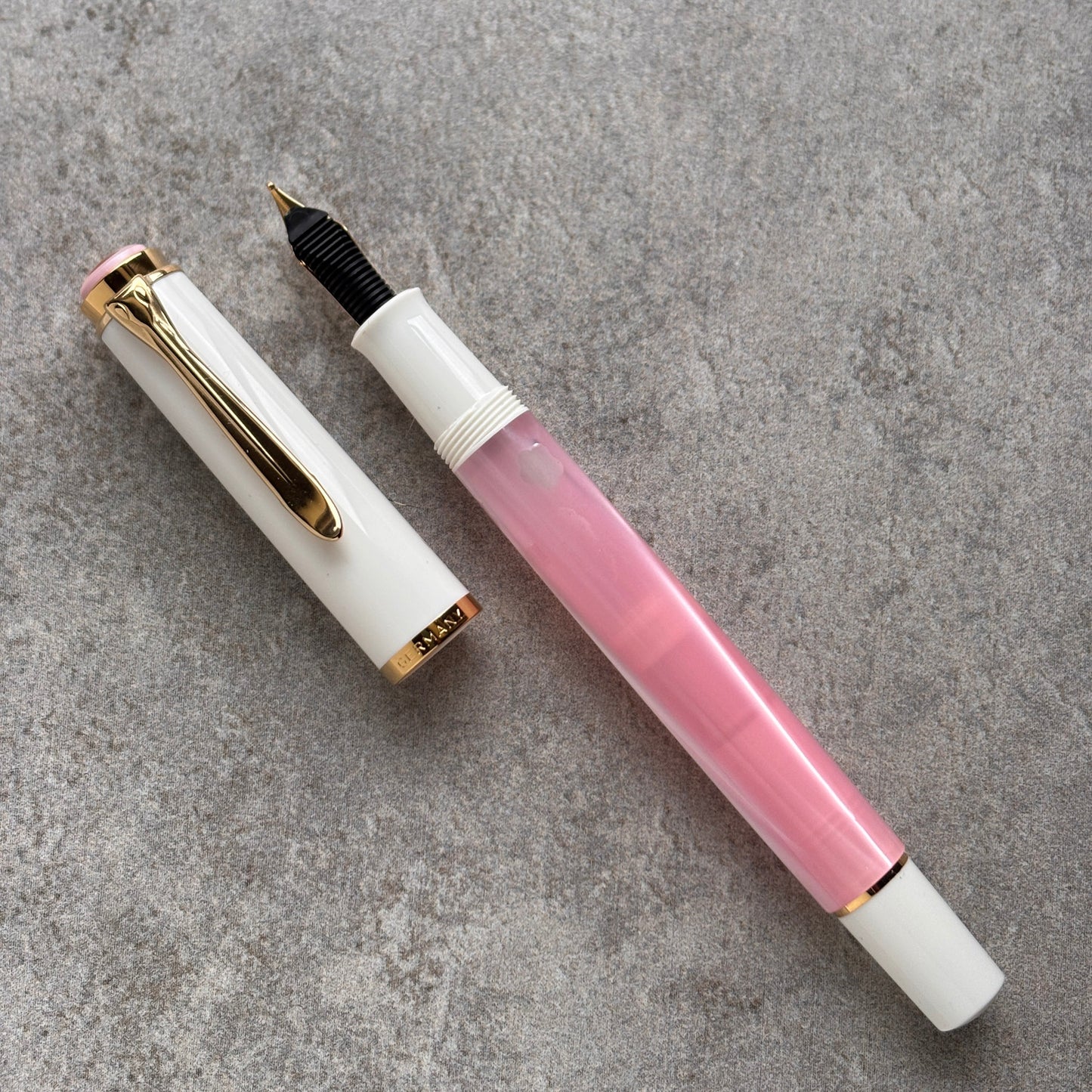 Two fountain pens, one white with gold accents and the other pink with a white cap, on a gray surface.