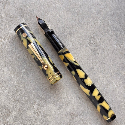 Fountain pen with black and yellow marbled design on a gray surface