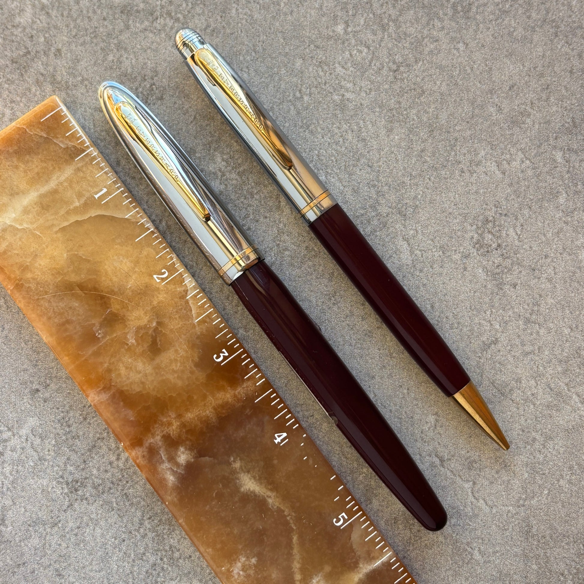 Two pens with gold accents on a stone surface next to a ruler.