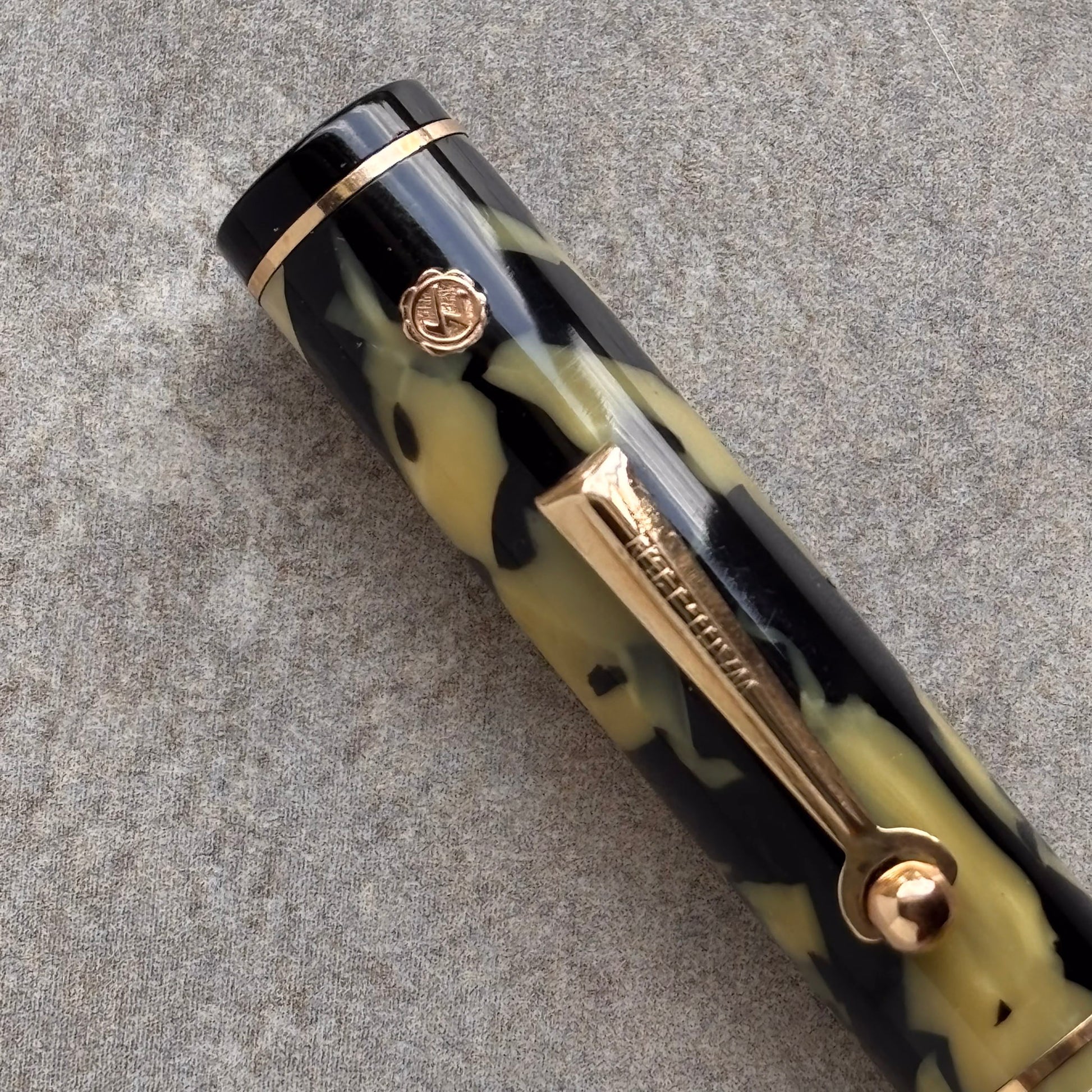 Camouflage-patterned pen with gold accents on a gray surface