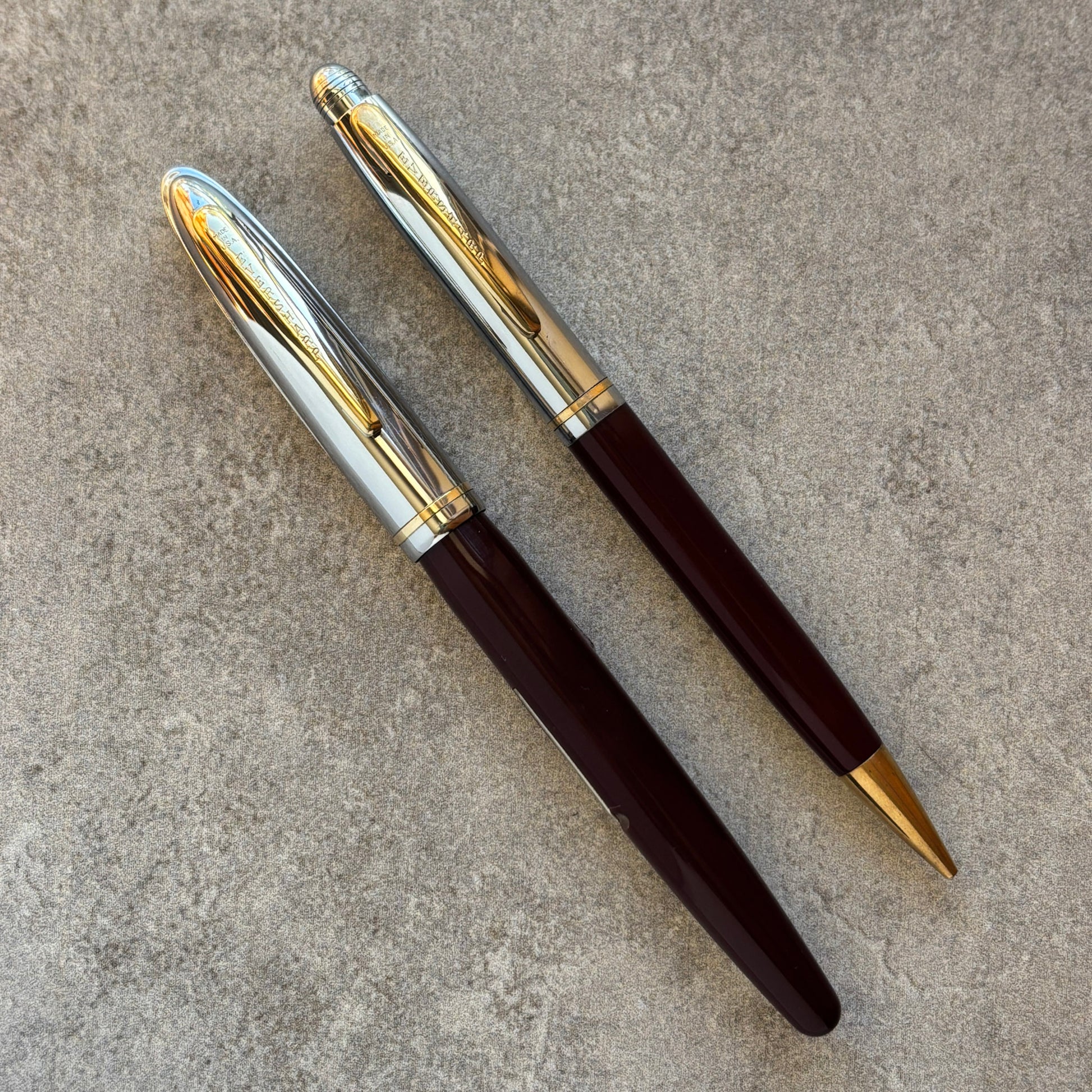 Two pens with gold and silver accents on a textured surface