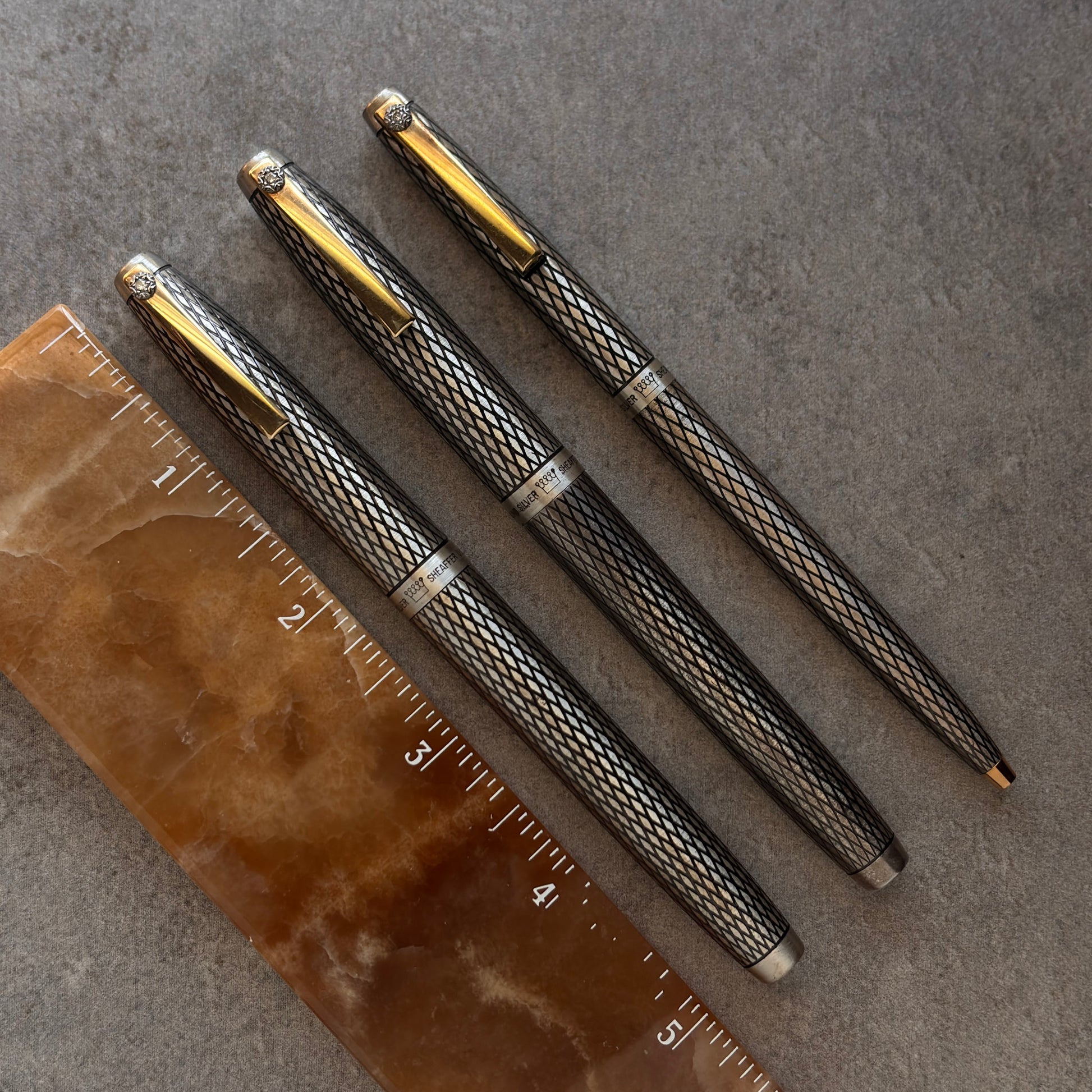 Three metallic pens with textured design on a gray surface with a ruler for scale.