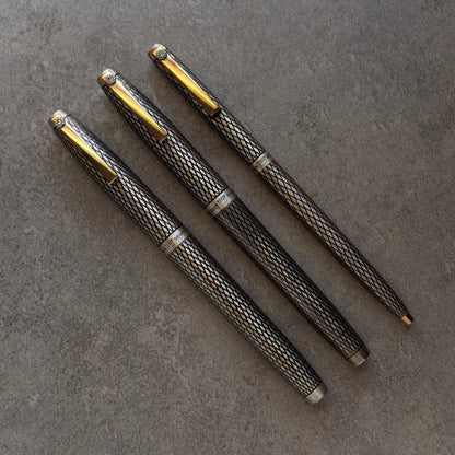 Three metallic pens with gold accents on a gray surface