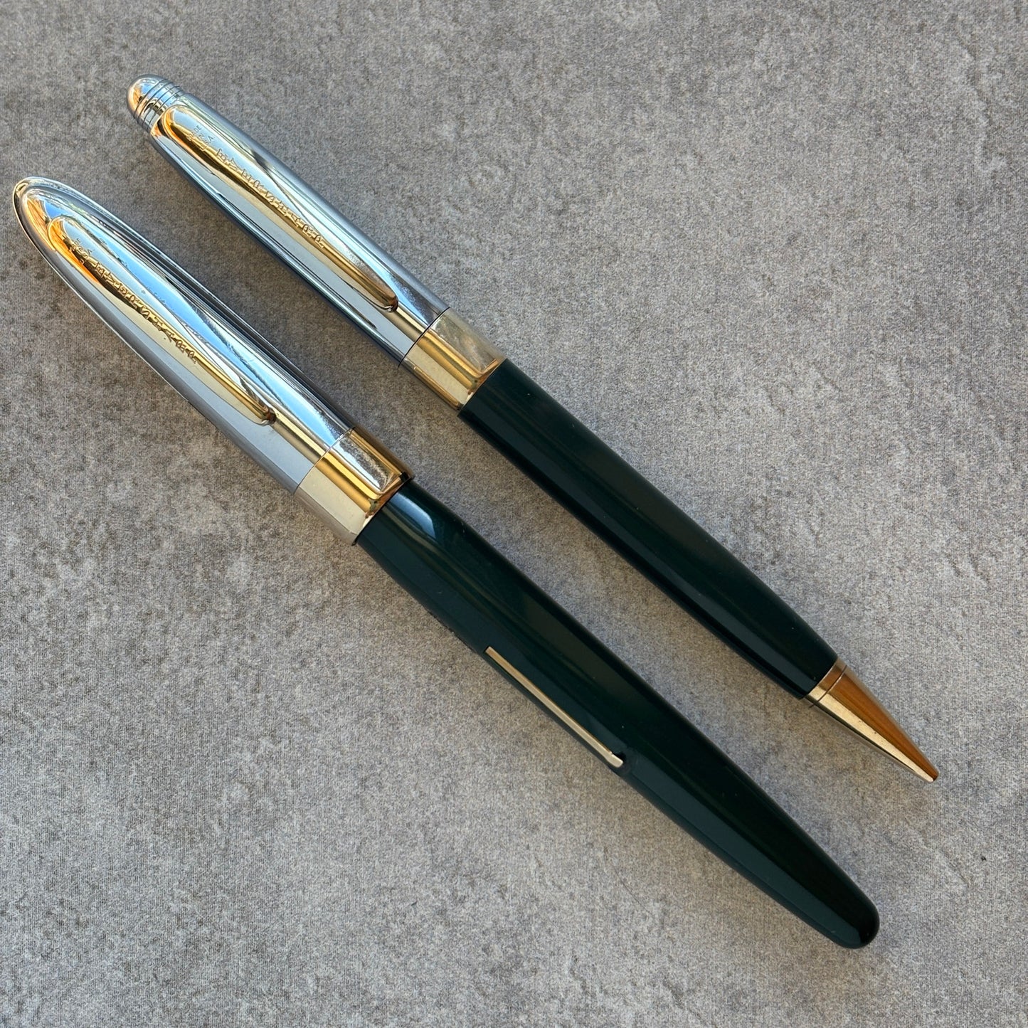 Pen with dark green body, gold accents, and silver clip on a gray surface