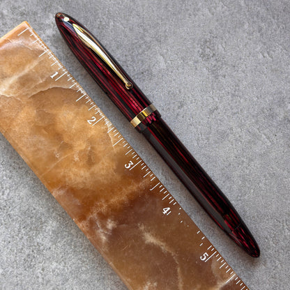 Red and gold pen on a brown stone surface with a ruler