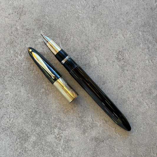 green and gold fountain pen on a gray concrete surface