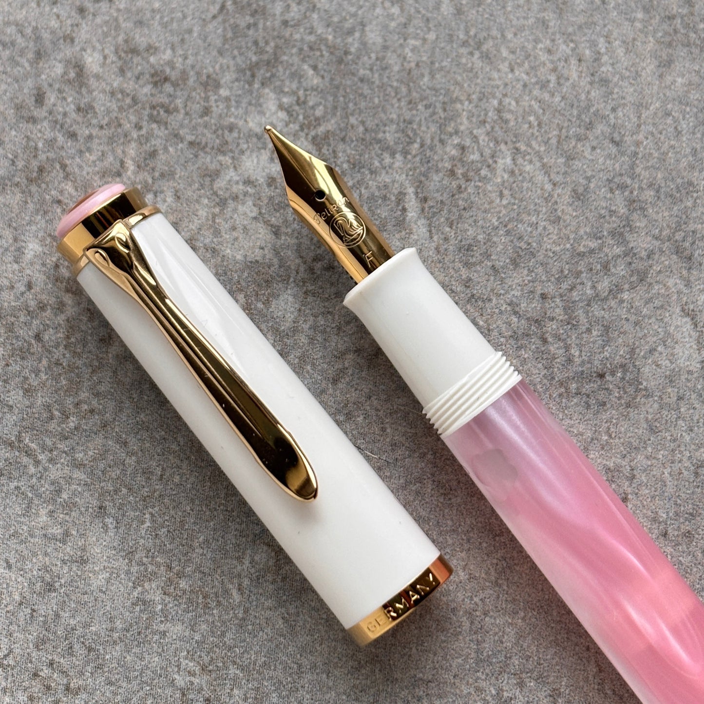 Fountain pen with white and pink body and gold accents on a gray background
