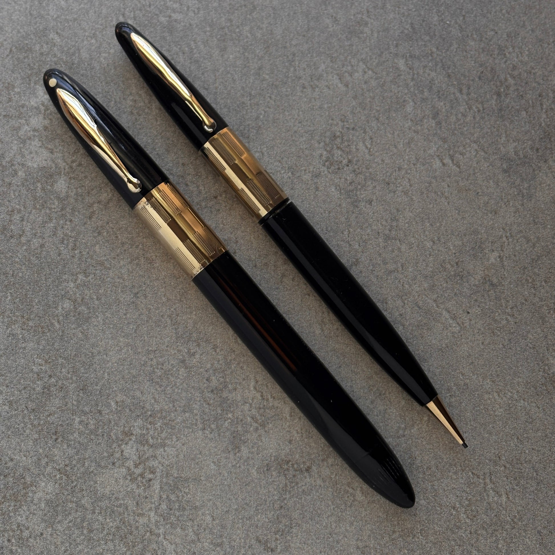 Two black and gold pens on a gray surface