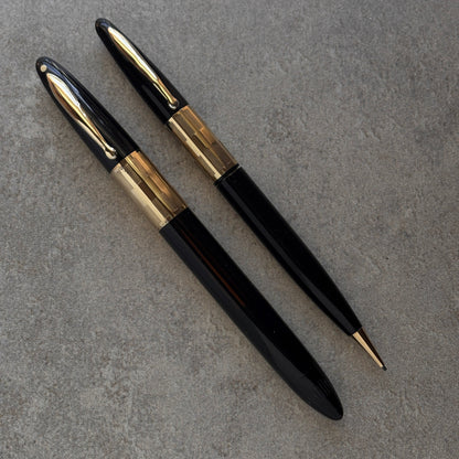 Two black and gold pens on a gray surface