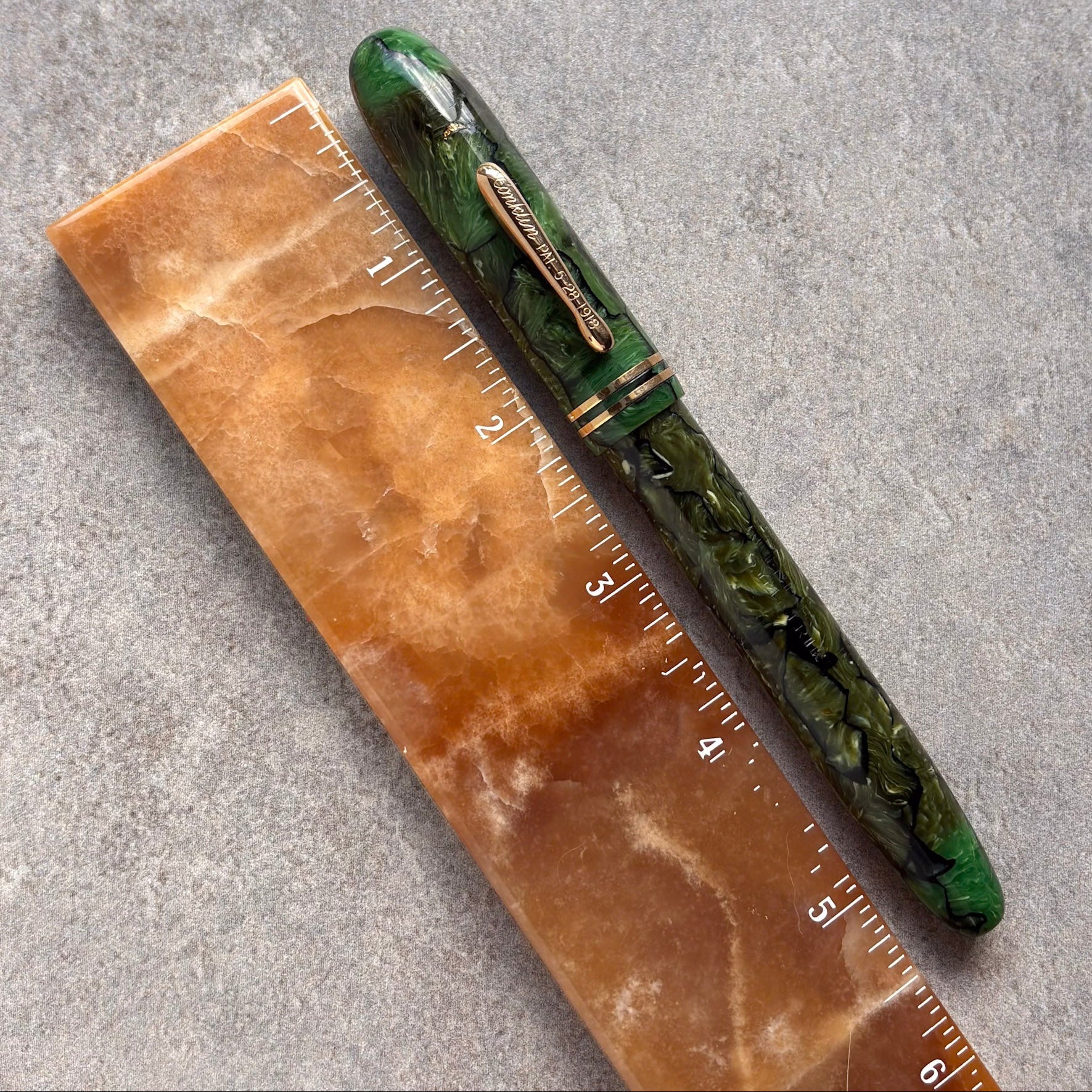 Green pen on a brown marble surface with a ruler for scale