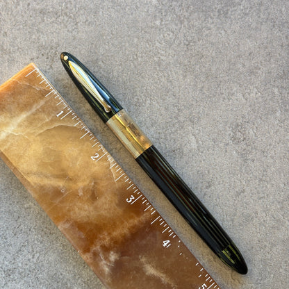 green and gold pen next to a ruler on a textured surface