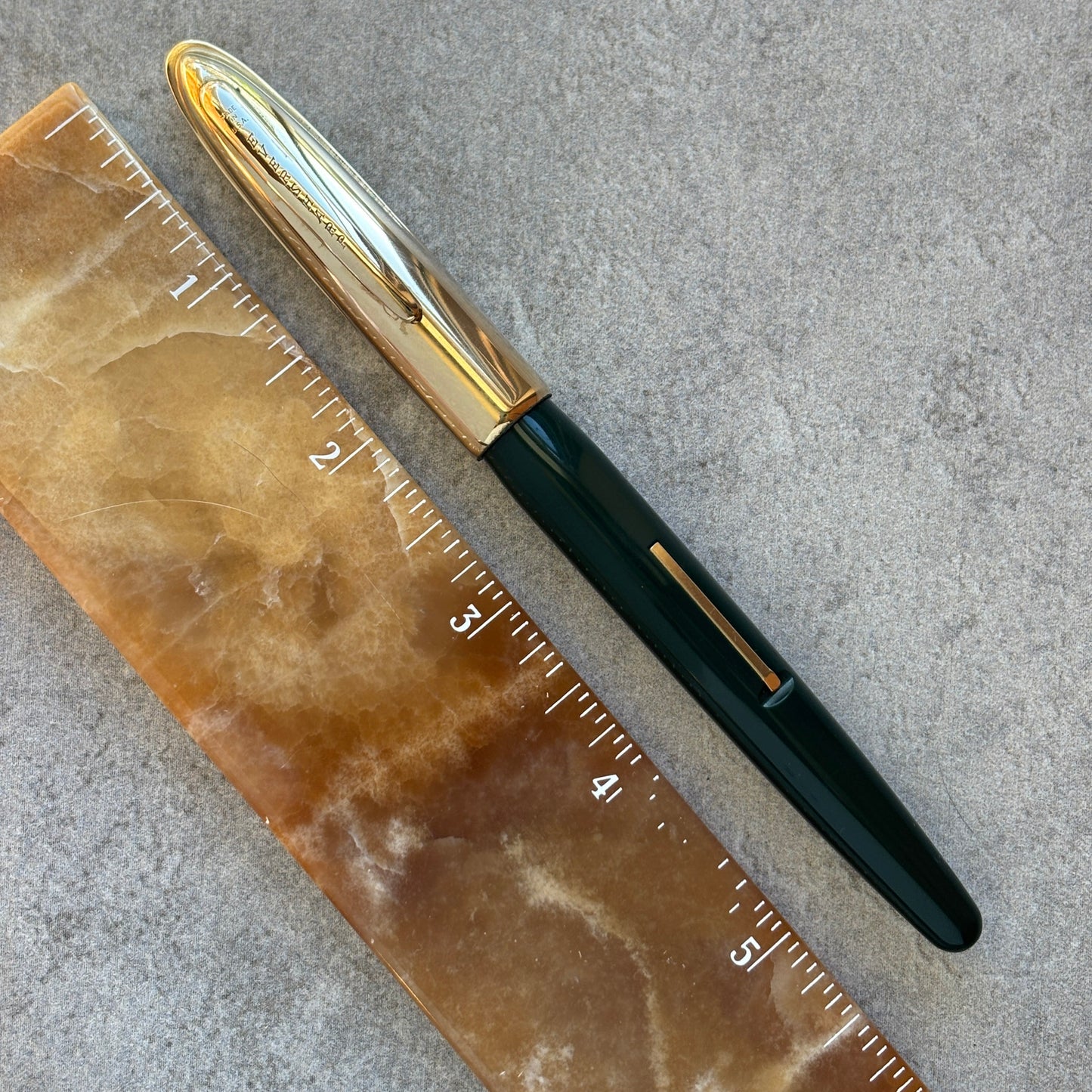 Fountain pen with gold accents next to a ruler on a textured surface
