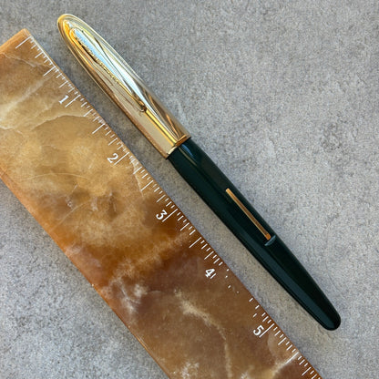 Fountain pen with gold accents next to a ruler on a textured surface