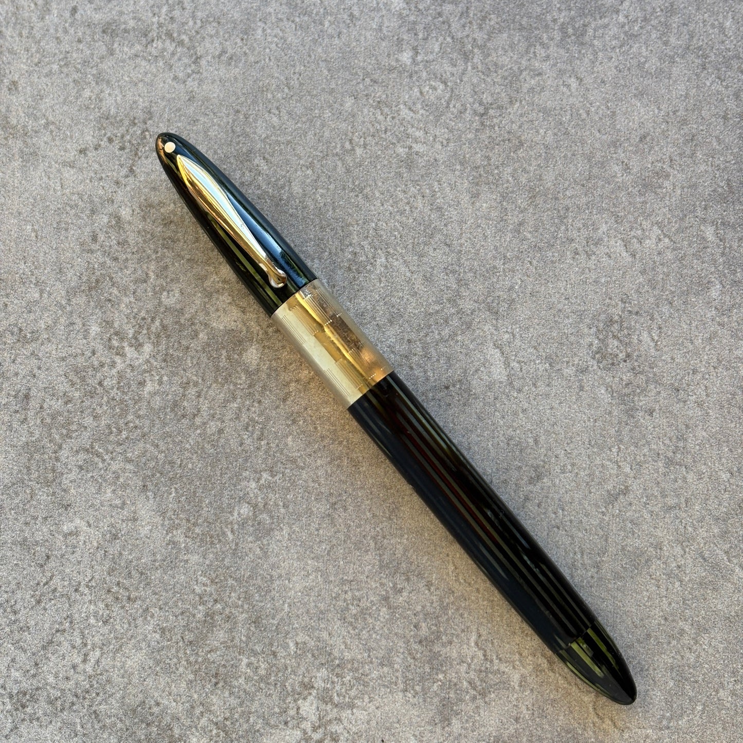 green and gold fountain pen on a gray concrete surface