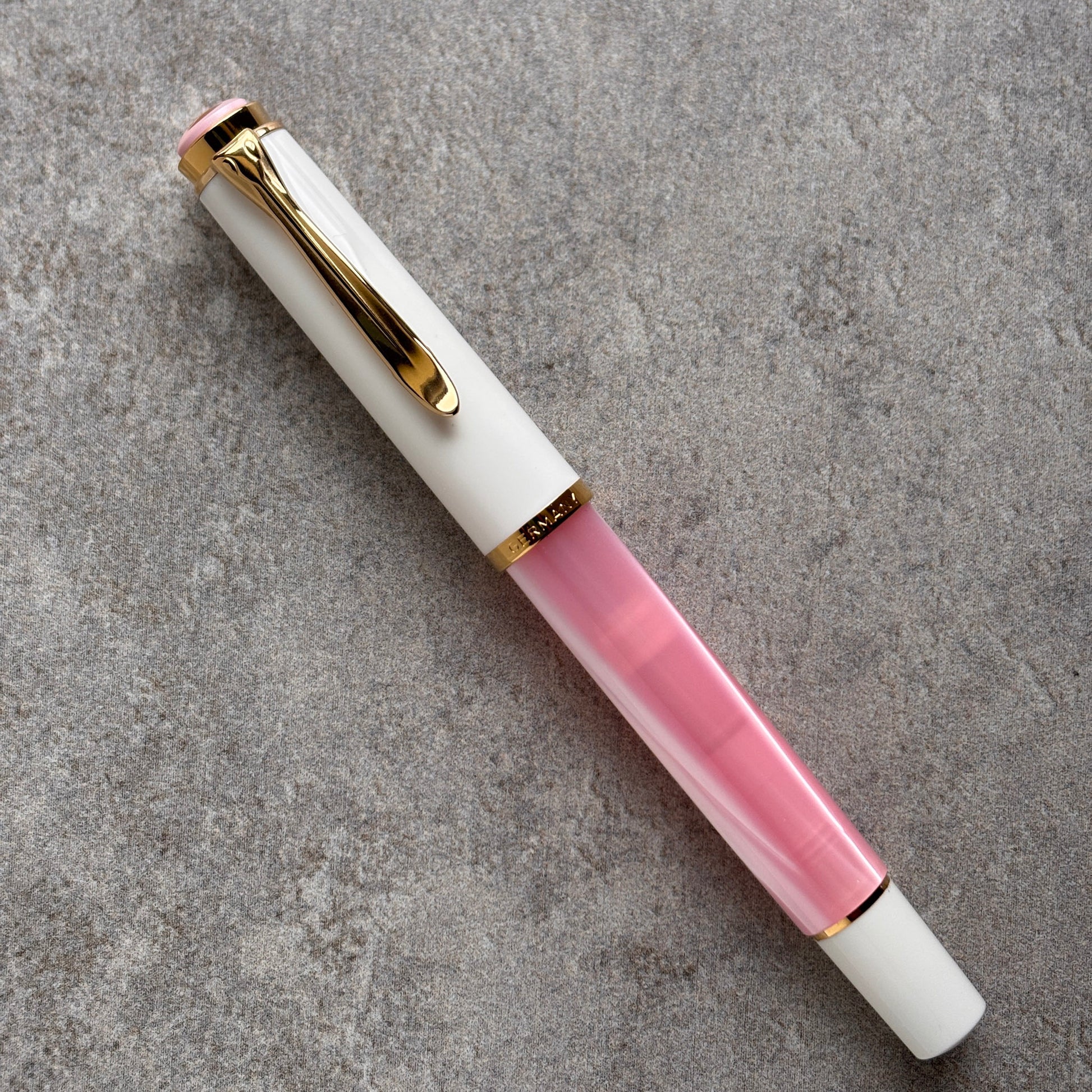 Pen with white and pink body and gold accents on a gray surface