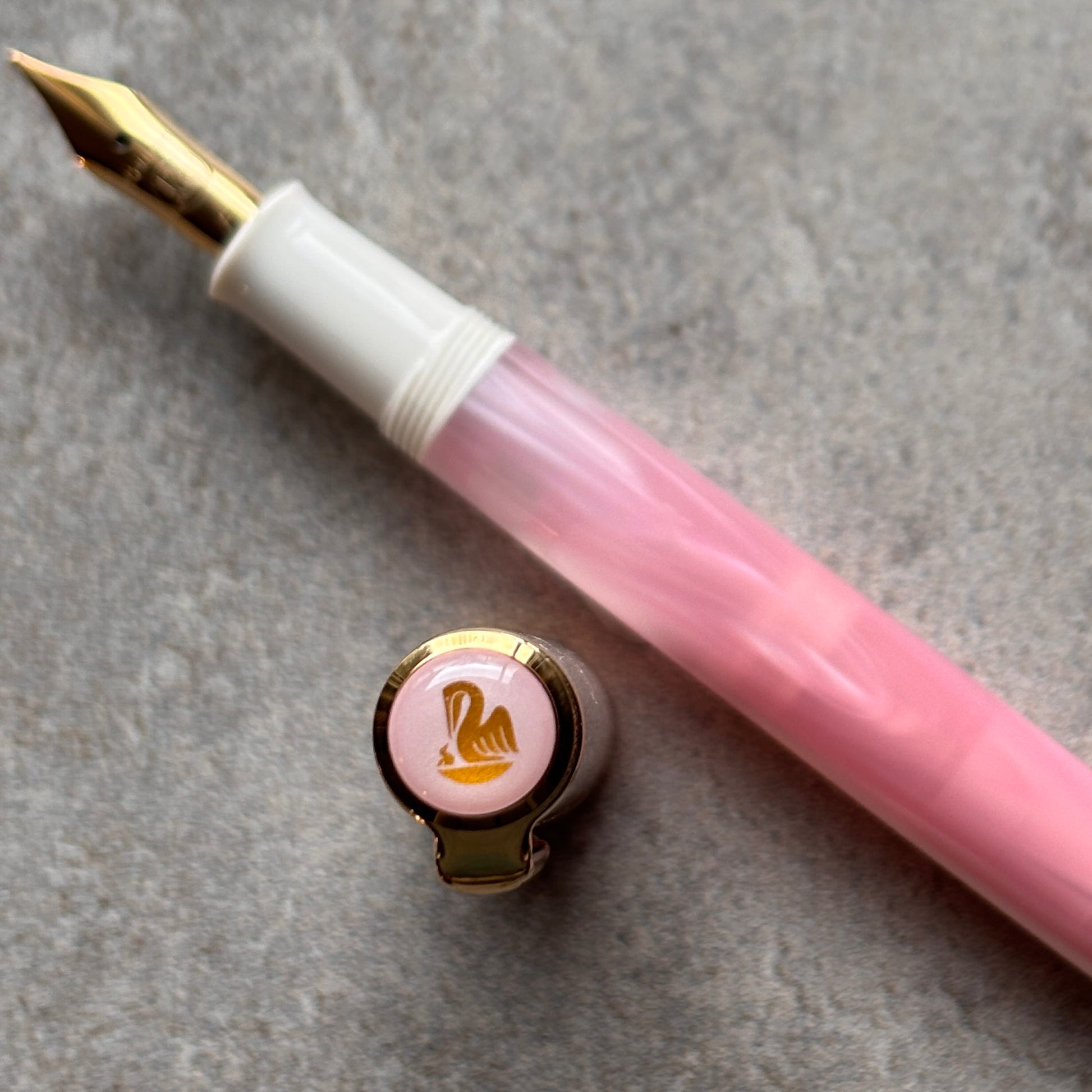 Pink fountain pen with gold accents on a gray surface