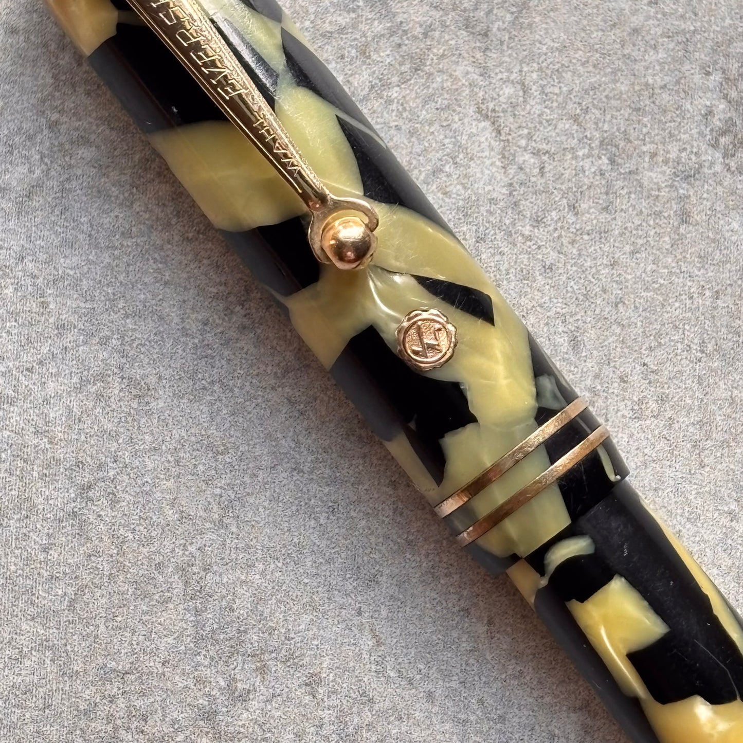 Close-up of a decorative pen with black, yellow, and gold pattern on a gray background
