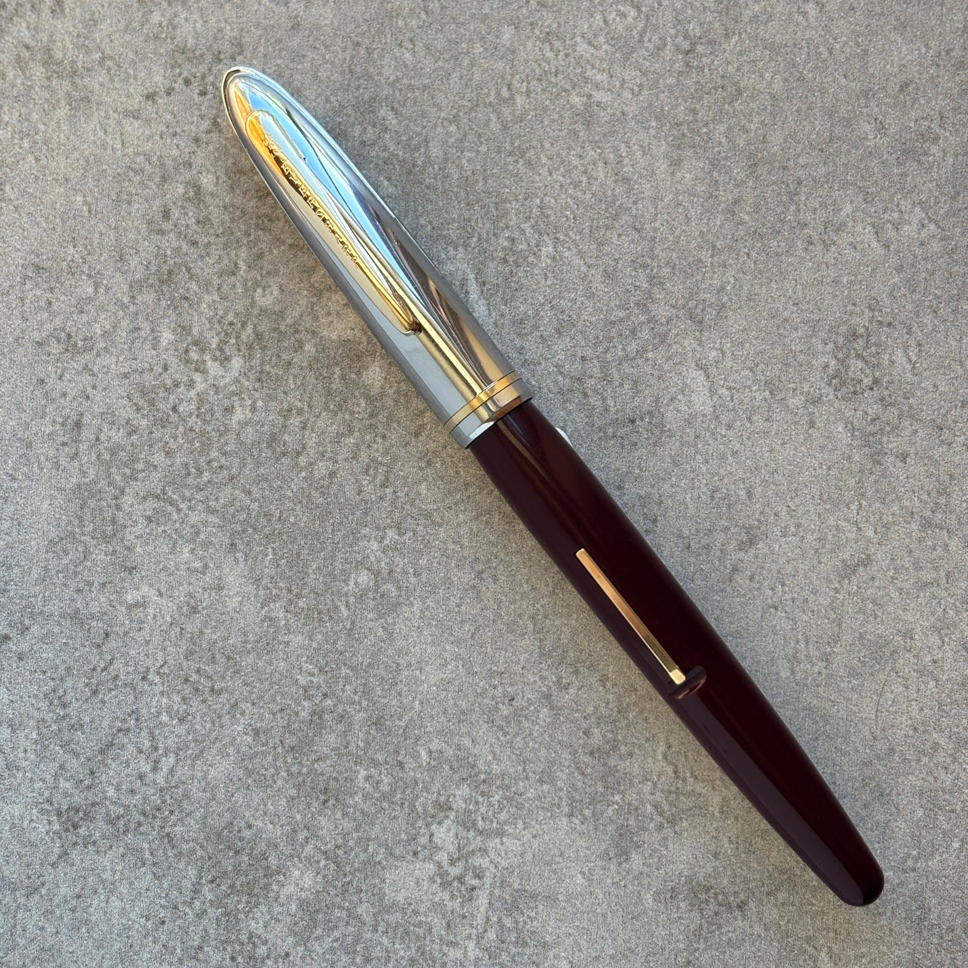 Fountain pen with a gold and silver cap on a gray concrete surface