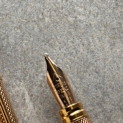 Close-up of a gold-toned fountain pen nib and part of the textured grip on a gray felt background.