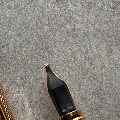 Close-up of a fountain pen nib and part of the gold-toned barrel resting on a textured gray felt surface.