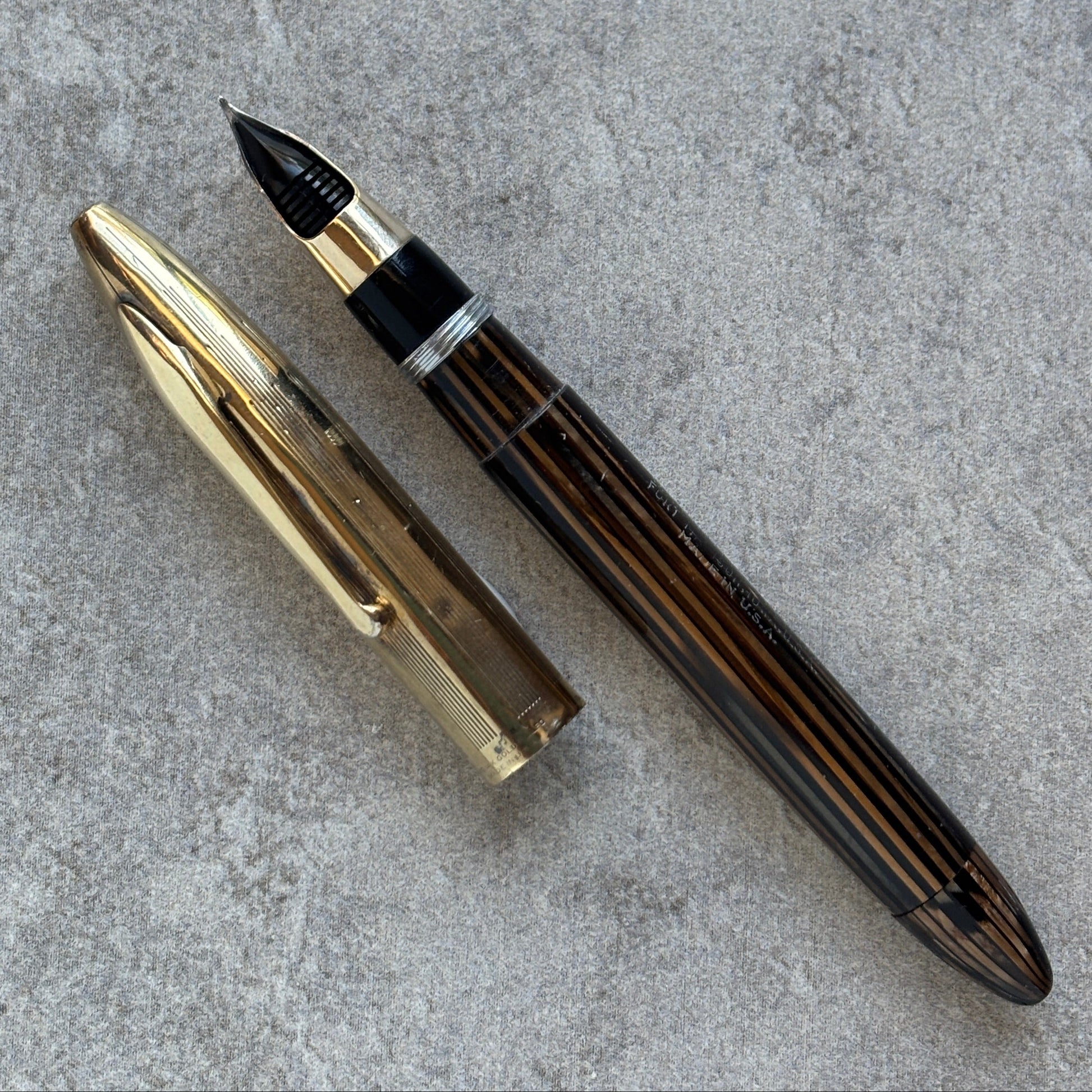 Fountain pen with gold cap and brown body on a gray surface