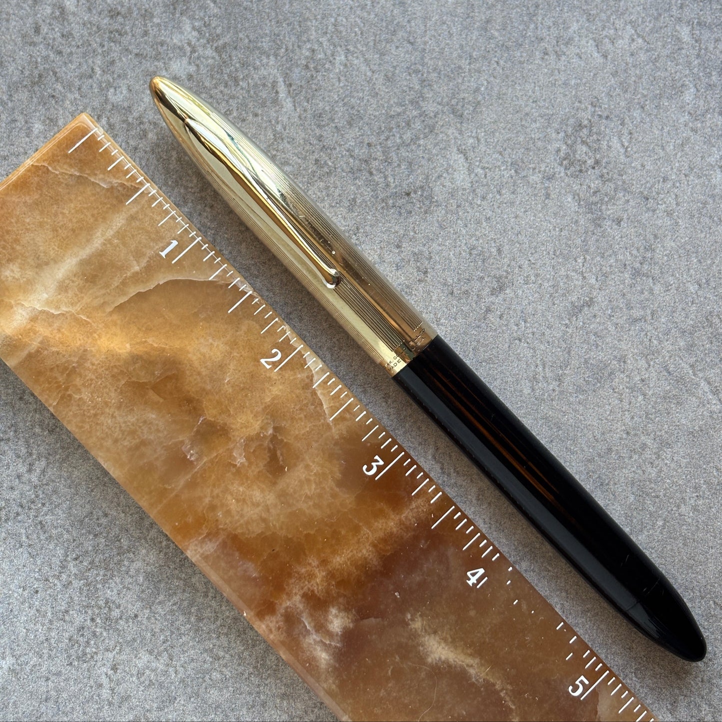 Pen with gold cap and black body on a marble ruler against a gray background