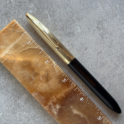 Pen with gold cap and black body on a marble ruler against a gray background