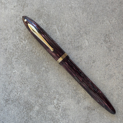 Fountain pen with a maroon or dark red body and gold accents on a gray concrete surface.
