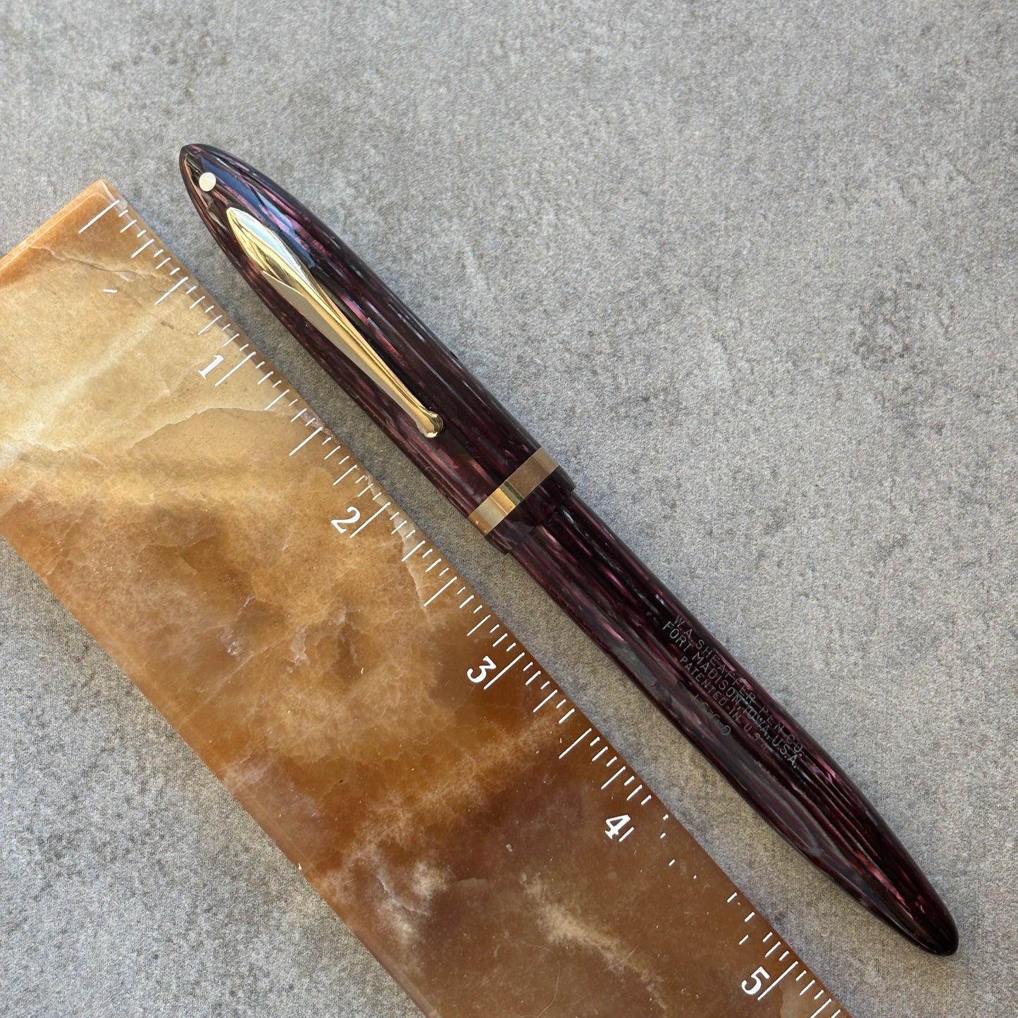 Maroon pen with gold clip on a ruler against a gray background