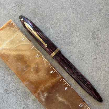 Maroon pen with gold clip on a ruler against a gray background