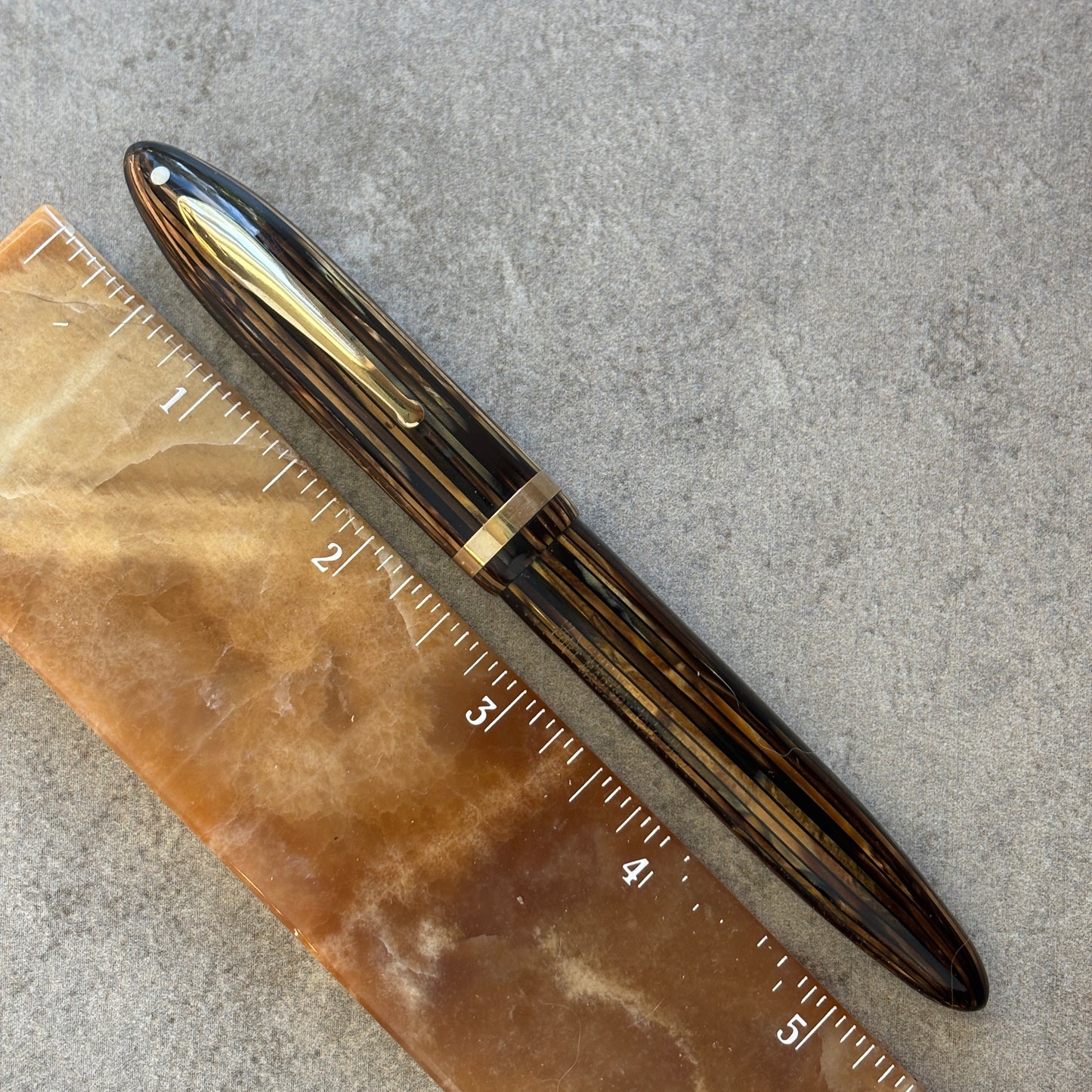 Gold pen on a textured surface with a ruler for scale