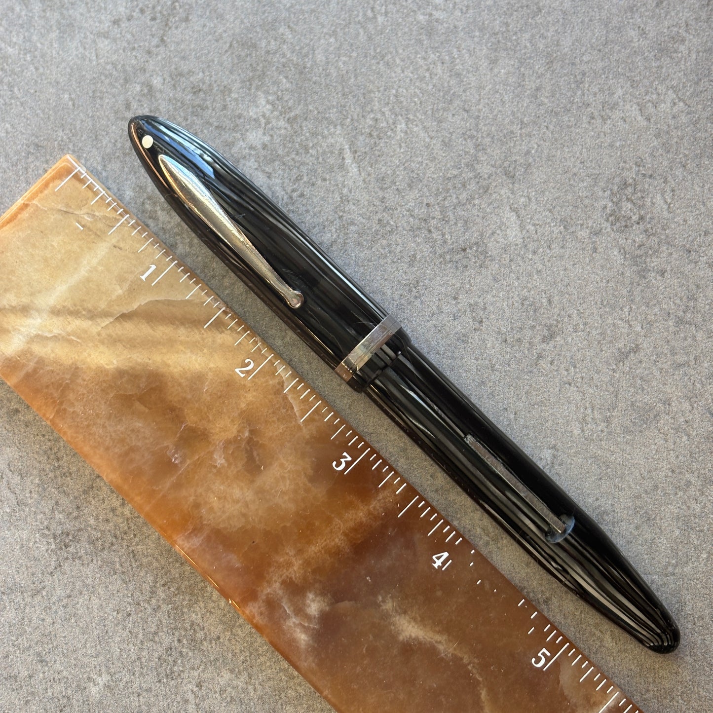 Grey Pearl pen next to a ruler on a gray surface