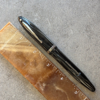 Grey Pearl pen next to a ruler on a gray surface