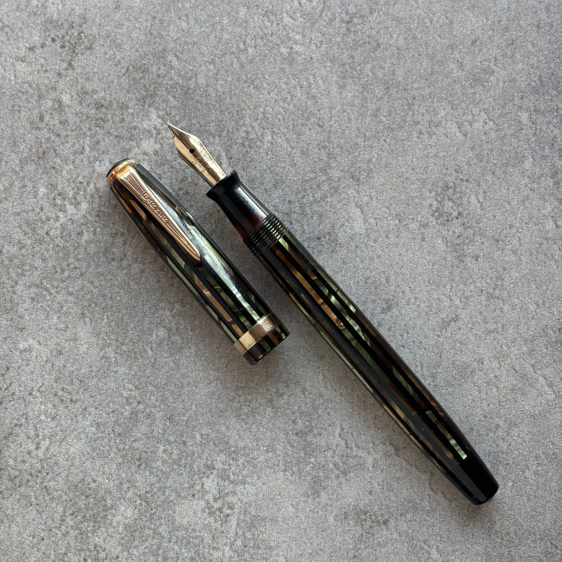 Green and gold Striped fountain pen on a gray concrete surface